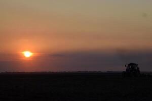 tractor arada arado el campo en un antecedentes puesta de sol. tractor silueta en puesta de sol antecedentes foto