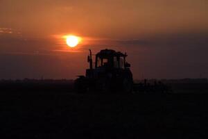 Tractor plowing plow the field on a background sunset. tractor silhouette on sunset background photo