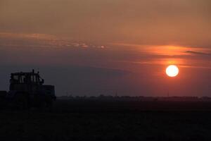 Tractor plowing plow the field on a background sunset. tractor silhouette on sunset background photo