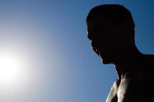 Silhouette of a man against a blue sky and sun. A man in drops of sea water photo