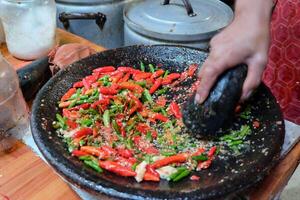 Female Hand Grinding red and Green Chilli on Stone Mortar photo