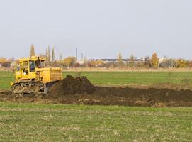 el amarillo tractor con adjunto grederom hace suelo arrasamiento. foto