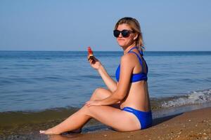 A blonde in sunglasses eats a watermelon by the sea. A juicy watermelon in the hands of a woman photo