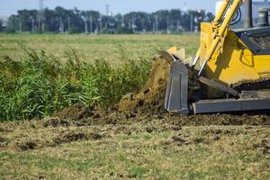 el amarillo tractor con adjunto grederom hace suelo arrasamiento. foto