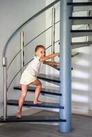 pequeño niño yendo arriba escalera a moderno hogar, niño alpinismo espiral escalera. peligroso situación a hogar. niño la seguridad concepto. foto