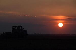 Tractor plowing plow the field on a background sunset. tractor silhouette on sunset background photo