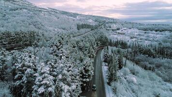 Antenne zum schneebedeckt Wald und ein und Auto ziehen um auf das Winter Straße. Schuss. Antenne Aussicht von das Straße durch ein Winter Wald mit ein ziehen um Fahrzeug auf wolkig Himmel Hintergrund. video