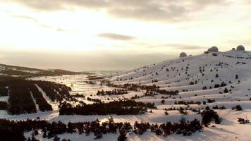 Aerial view of the astrophysical observatory in wintertime in snowy forest, Crimea. Shot. Beautiful landscape of snowy pine trees, observatory on sunset, cloudy sky background. video