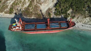 Aerial top view of an empty, red barge moored near the beautiful blue sea shore. Big Industrial ship standing near the hill with green trees. video