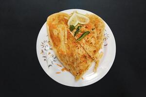 paratha servido con pepino, verde chile, zanahoria, y cilantro hojas, corazón firmar paratha en un blanco plato en un negro antecedentes foto