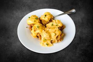 Fried chicken benedict topped with Hollandaise sauce. Chicken fried, Pumpkin sauce, butter on a white plate on a black background photo