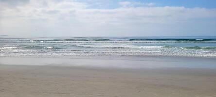 imagen de playa con blanco arena y calma mar en soleado día con bañistas y surfistas en el playa foto