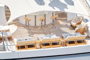 Close up footage of a relaxation area on the open teak deck of an expensive megayacht at sunny day, with awnings stretched over the deck to protect from the sun, wealth life, table and chairs photo