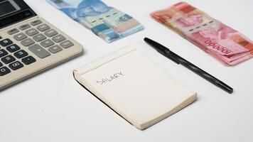 photo of salary notes, calculator, and rupiah banknotes on a white background