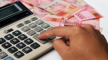 hand pressing a calculator with a collection of Indonesian banknotes photo