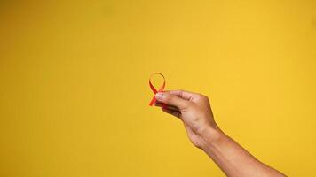 hand holding a red HIV ribbon on a yellow background photo