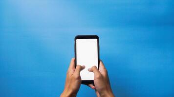 Two hands holding smartphone with blank screen mockup frame, isolated on blue background photo