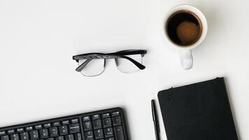 workspace desk with notebooks, pens, keyboard, glasses and coffee on white background photo