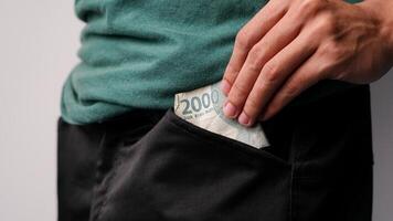 A man's hand is putting 2000 rupiah in his trouser pocket for savings photo