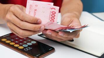 a man's hand is counting rupiah money with a calculator and notes photo
