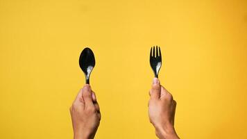 Man's hand holding a black spoon and fork on a yellow background photo