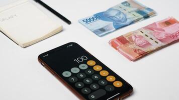 close up of a calculator and rupiah banknotes and notes on a white background photo