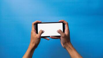 Hand of man holding mobile smartphone with gesture playing game on blue background photo