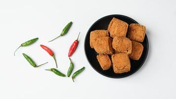 Fried tofu on a black plate with chilies in a white background photo