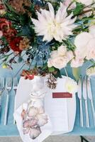 Invitation on a plate near the cutlery on the table next to the bouquet. Top view photo