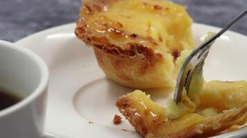 comendo com uma sobremesa garfo uma fresco e quente crocantes sopro pastelaria torta com ovo creme em uma branco prato às café da manhã dentro uma cafeteria com café. Português sobremesa pastel de nata ou pastel de Belém. video