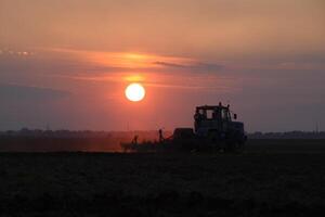 Tractor plowing plow the field on a background sunset. tractor silhouette on sunset background photo