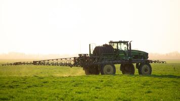 tractor en el puesta de sol antecedentes. tractor con alto ruedas es haciendo fertilizante en joven trigo. foto