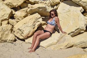 The dark-haired girl in a swimsuit on the yellow rocks photo