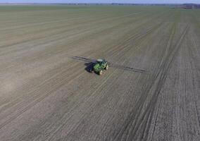 Tractor with hinged system of spraying pesticides. Fertilizing with a tractor, in the form of an aerosol, on the field of winter wheat. photo