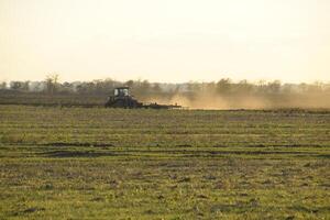 Tractor at sunset plow plow a field. Tilling the soil in the fall after harvest. The end of the season photo
