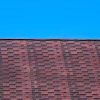 Roof from multi-colored bituminous shingles. Patterned bitumen shingles. Bituminous burgundy roof. photo