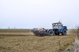 lozano y aflojar el suelo en el campo antes de siembra. el tractor arados un campo con un arado foto