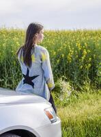 A girl with a bouquet of daisies sits on the hood of the car and photo