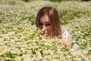 A woman in a white dress with polka dots is on a glade with daisies. Blooming daisies photo