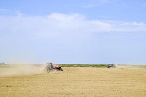 Tractor with a grader aligns the soil on the field. The tractor raised dust. photo