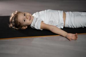 pequeño niña relajarse y meditar acostado en el estera mientras practicando yoga en oscuro habitación foto