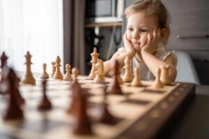 Little girl playing chess at the table in home kitchen. The concept early childhood development and education. Family leisure, communication and recreation. photo