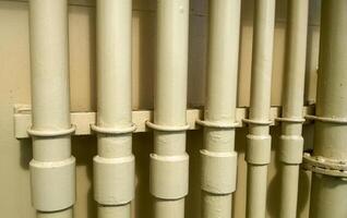 White pipes near the wall. Flanged connection on a gray pipe. Pipes on the deck of the ship photo