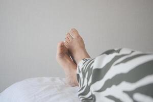 young Woman lying with bare feet in bed, photo