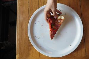 top view of hand picking slice of pizza from a plate photo