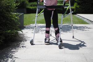 child with walking frame and knee orthosis outdoor photo