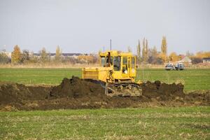 el amarillo tractor con adjunto grederom hace suelo arrasamiento. foto