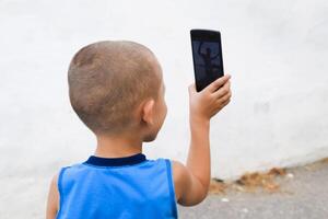 niño con un teléfono inteligente un pequeño chico dispara vídeo en un teléfono inteligente foto