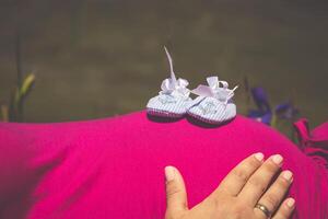 Pregnant woman lying on a grass with baby shoes on her belly photo