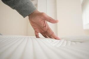 Hand touching and pressing orthopedic mattress on bed. photo